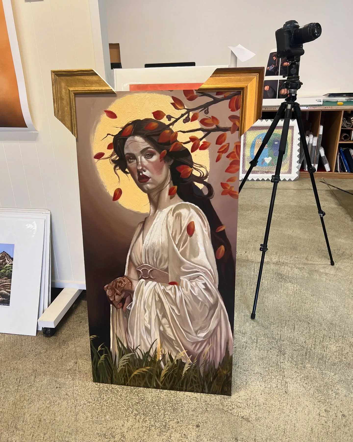 Oil painting of a woman in white with a gold halo and red leaves