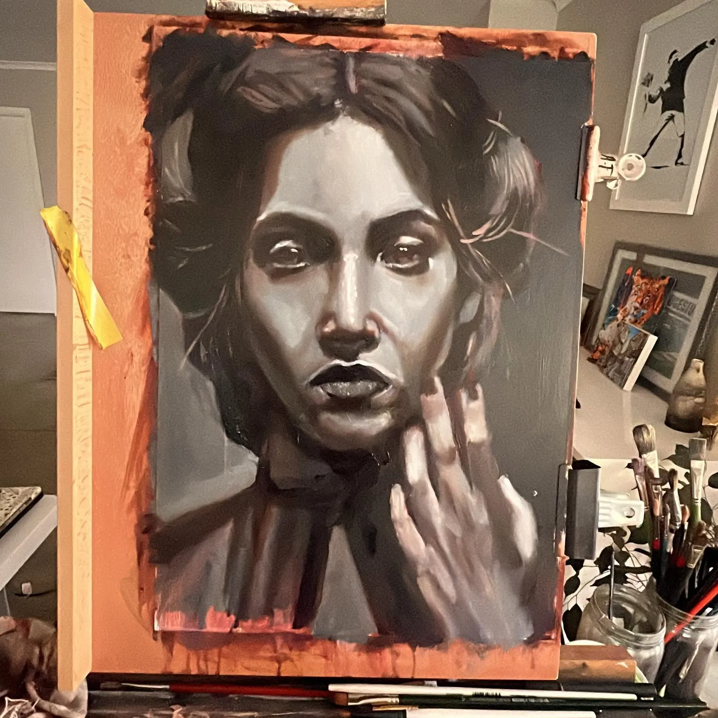Oil painting of a woman with her hand to her face, in grey tones, on the easel