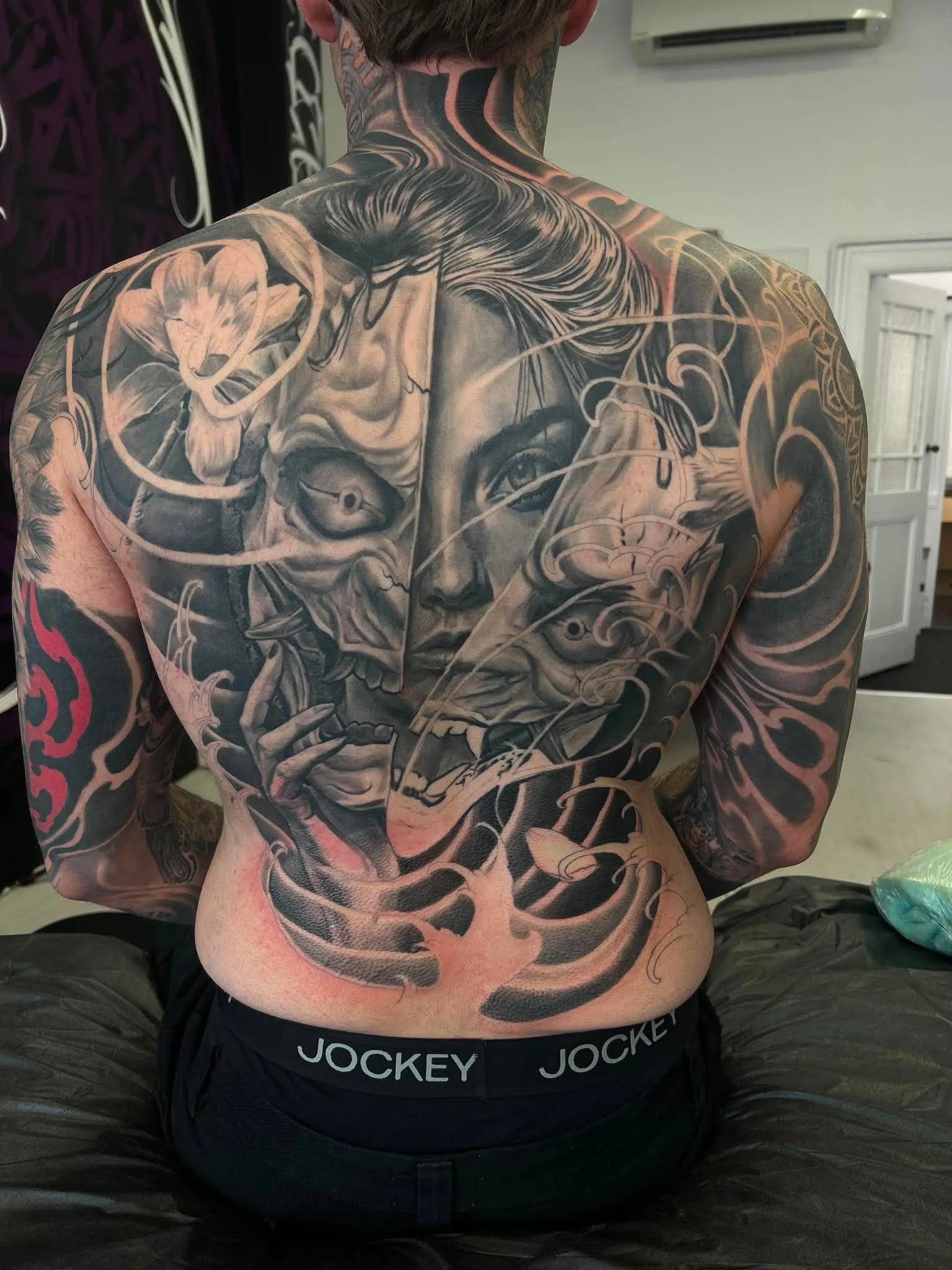 Full back piece in black and grey realism with faces and flowing hair